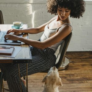 Young woman working from home on a laptop with her dog, embodying modern freelance lifestyle.